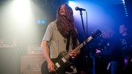 Gitarrist mit langen Haaren schaut beim Spielen zur Seite