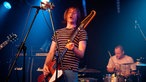 Bassist mit offenem Mund im Vordergrund, Schlagzeuger im Hintergrund