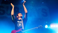 Billy Lunn hat seine Gitarre umhängen und  klatscht in die Hände