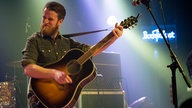 Akustikgitarrist von Tim Vantol schlägt einen schönen Akkord auf seiner Gitarre an und schaut ehrgeizg zur Seite
