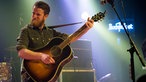 Akustikgitarrist von Tim Vantol schlägt einen schönen Akkord auf seiner Gitarre an und schaut ehrgeizg zur Seite