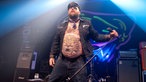 Der Frontmann steht auf der Bühne und lässt einen seinen Bauch mit dem Tigertatoo sehen.