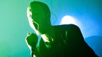 Sänger singt mit weit geöffnetem Mund im blaugrünen Bühnenlicht.