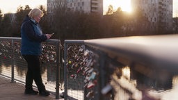 Frau steht auf Brücke, im Hintergrund geht die Sonne unter.