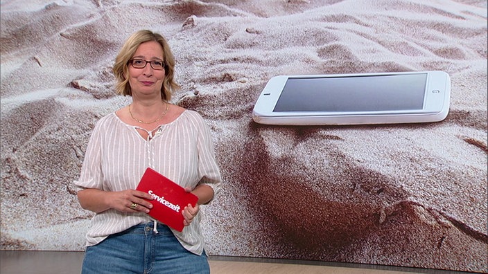 Yvonne Willicks steht im Serviczeit-Studio. Im Hintergrund sieht man eine Nahaufnahme von einem Handy am Strand.
