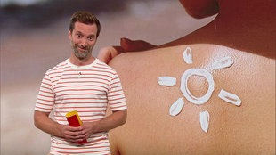 Daniel Aßmann steht im Servicezeit-Studio. Im Hintergrund sieht man eine Nahaufnahme einer Schulter, auf die ein Motiv aus Sonnencreme gemalt wurde.
