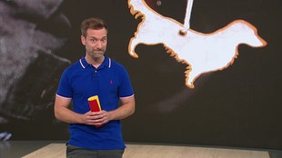 Daniel Aßmann steht im Servicezeit-Studio. Im Hintergrund sieht man eine Nahaufnahme eines refklektierenden Schlüsselanhängers.
