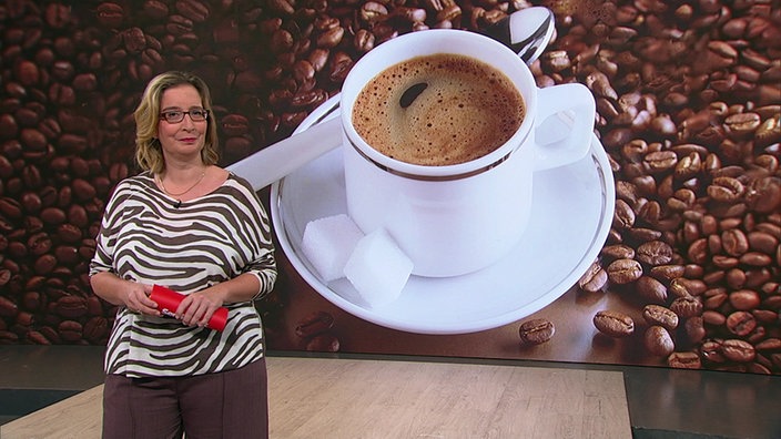 Yvonne Willicks steht im Servicezeit-Studio. Im Hintergrund sieht man eine Grafik, in der eine Kaffeetasse umrandet von Bohnen dargestellt wird.