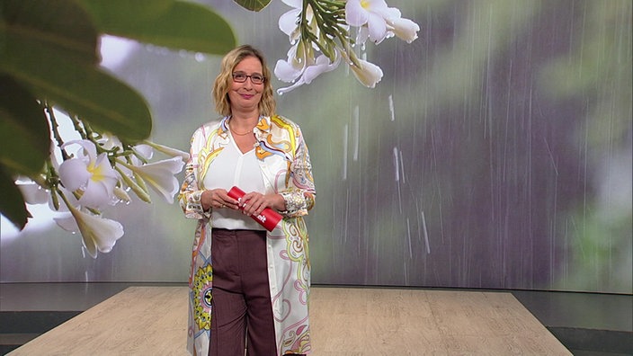 Yvonne Willicks im Servicezeit-Studio im Hintergrund eine regnerische Kulisse.