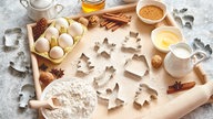 Weihnachtliches Bild mit Austechförmchen und Zutaten für Plätzchen.