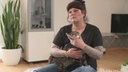 Eine Frau mit dunklen Haaren hat eine Katze bei sich auf dem Schoß 