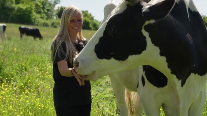 Eine blonde Frau streichelt eine Kuh auf einer Weide 