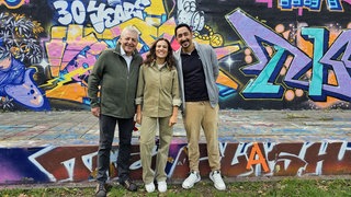 Musical "Baha und die wilden 70er": Siham El-Maimouni mit Nedim Hazar (li.) und Eko Fresh vor einer Wand mit Graffiti