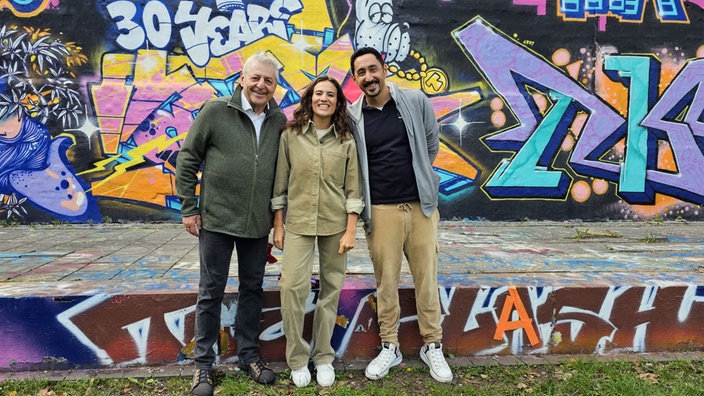 Musical "Baha und die wilden 70er": Siham El-Maimouni mit Nedim Hazar (li.) und Eko Fresh vor einer Wand mit Graffiti
