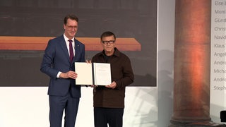 Zwei Männder stehen auf einer Bühne und halten gemeinsam eine Urkunde