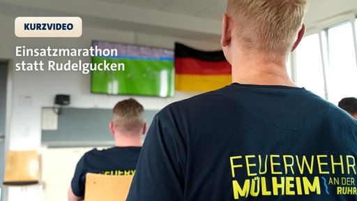 Rücken eines Feuerwehrmannes mit Blick zum Fernseher. Dort läuft das WM-Spiel der Nationalmannschaft.