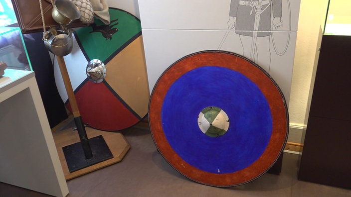 Ein rot-blaues rundes römisches Schild lehnt an der Wand