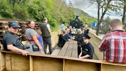 Brohtalbahn: Fahrgäste sitzen und stehen im offenen Wagon hinter der Dampflok.