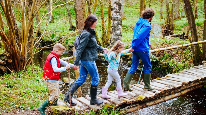 Eine Familie überquert bei einer Wanderung einen Bach auf einer Holzbrücke.