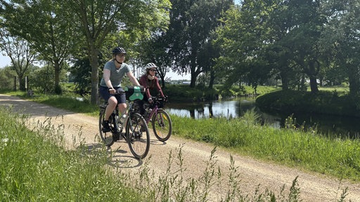 Zwei Radlerinnen fahren nebeneinander auf einem Radweg, der direkt neben der Rur verläuft 