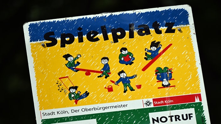 Ein großes Schild mit der Aufschrift Spielplatz. Auf dem Schild sind Bilder von spielenden Kindern.