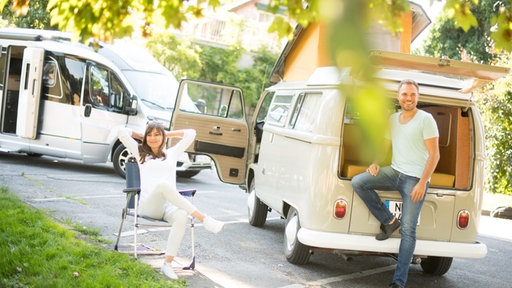 Mann und Frau vor neuem Wohnmobil und Retro-Bully