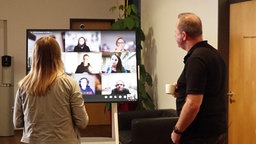 Das Bild zeigt zwei Angestellte bei einem Videoanruf mit Kollegen.
