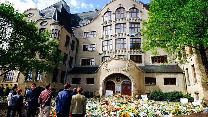 Vor dem Gutenberg-Gymnasium in Erfurt liegen viele Blumen. Menschen haben sich vor dem Gebäude versammelt, um den Opfern zu gedenken.