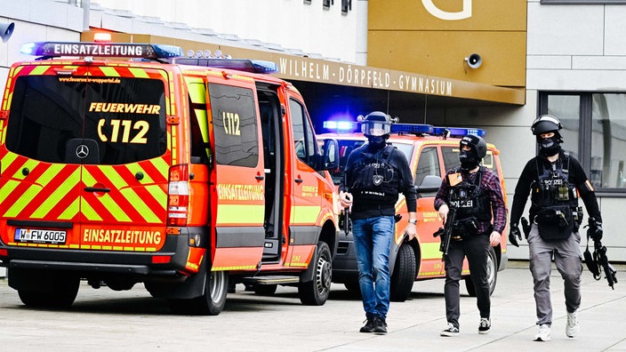 Einsatzwagen und drei bewaffnete, uniformierte Polizisten stehen vor dem Wilhelm-Dörpfeld-Gymnasium.