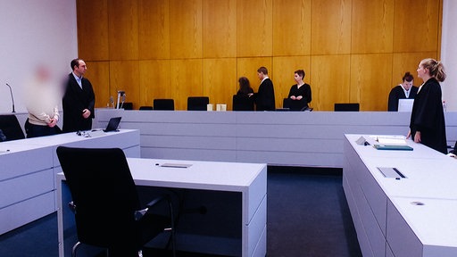 Der Beginn einer Gerichtsverhandlung, Richter, Angeklagter und Anwalt im Gerichtssaal, der Angeklagte ist unkenntlich gemacht