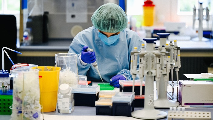 Ein Rechtsmediziner in Arbeitskleidung. Er befindet sich in einem Labor und hält eine Pipette in der Hand