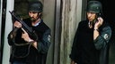 Zwei Polizisten in Schutzausrüstung stehen an der Sparkasse. Einer hält eine Schusswaffe in der Hand.