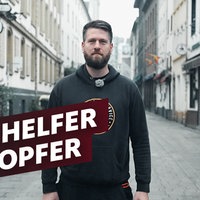 Ein Mann steht in der Düsseldorfer Altstadt und guckt in die Kamera. Auf dem Foto der Schriftzug "Vom Helfer zum Opfer"