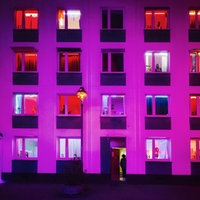 Sexarbeitende befinden sich hinter den Fenstern eines pink und rot erleuchteten Bordells.