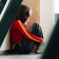Eine junge Frau, Sarah Rexin sitzt auf dem Boden und lehnt einer Wand. Man sieht ihr Gesicht nicht.
