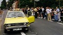 Das verunfallte Auto der Ehefrau eines Täters. Daneben stehen Polizisten und hinter einer Absperrung zahlreiche Schaulustige.