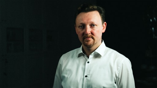 Ein Mann mit dunklen Haaren im Hemd schaut in die Kamera.