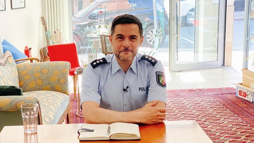 Volkan Eren sitzt in Polizeiuniform an einem Tisch.