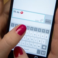 Eine Frau tippt auf einem Smartphone "Hi du" und einen Kussmund ein