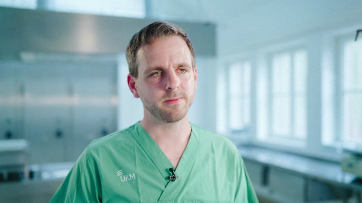 Dr. Maximilian Hagen in seiner Arbeitskleidung. Er befindet sich in einem Untersuchungszimmer.