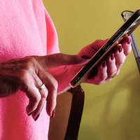 Eine Frau hält ein Handy in ihrer linken Hand. Mit der rechten Hand scrollt sie auf dem Bildschirm.