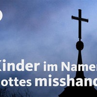 Ein Kreuz, dahinter ein bewölkter Himmel. Rechts ist ein Baum ohne Blätter.