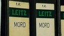 Gelb-Schwarzer Leitz-Ordner mit grüner Aufschrift "LEITZ", da drüber steht in schwarzer Schrift auf gelbem Grund "1.K.", darunter "MORD"