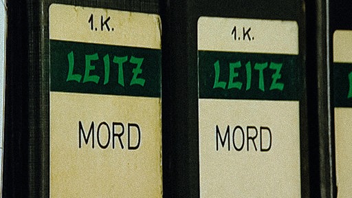 Gelb-Schwarzer Leitz-Ordner mit grüner Aufschrift "LEITZ", da drüber steht in schwarzer Schrift auf gelbem Grund "1.K.", darunter "MORD"