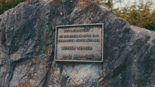 Auf einer Plakette auf dem Gedenkstein steht "Zur Erinnerung an unseren am 25.06.1995 ermordeten Jagdkameraden Werner Senger, seine Jagdfreunde"
