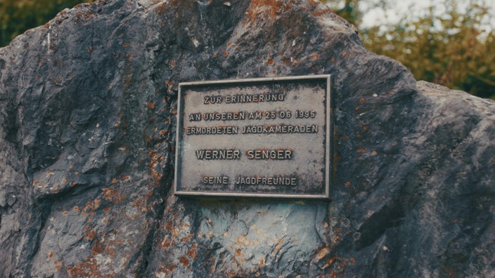 Auf einer Plakette auf dem Gedenkstein steht "Zur Erinnerung an unseren am 25.06.1995 ermordeten Jagdkameraden Werner Senger, seine Jagdfreunde"