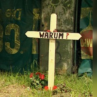 Archiv-Bild: Auf einer Grünfläche steht ein Kreuz aus Holz. Darauf steht in großer Schrift "WARUM?"