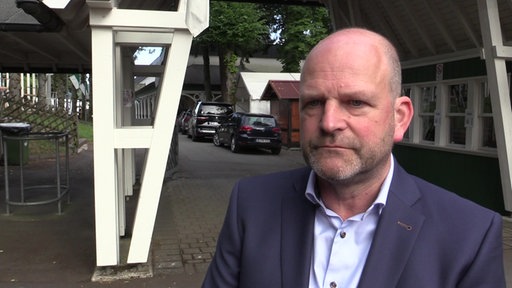 Andreas Roll steht auf dem Bürgersteig einer Straße. Links neben ihm der Eingang zum Schützenverein