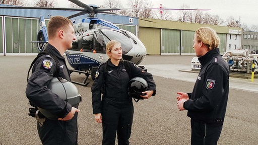 Lisa Ocklenburg unterhält sich mit zwei weiteren Polizisten. Im Hintergrund ein Helikopter der Polizei.