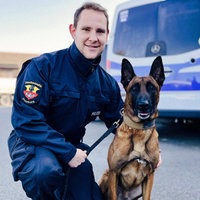 Gregor Köpp kniet neben dem sitzenden Spürhund Cash.